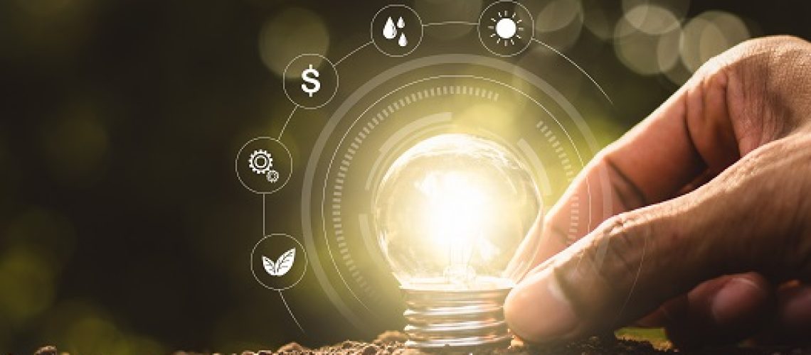 The light bulb was placed on the ground and there was a man's hand holding while there was a technology icon around it.