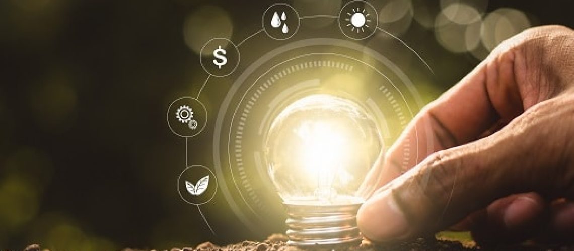 The light bulb was placed on the ground and there was a man's hand holding while there was a technology icon around it.