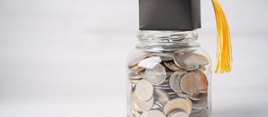 Graduation gap hat on coins money in jar for education fund; study learning concept.