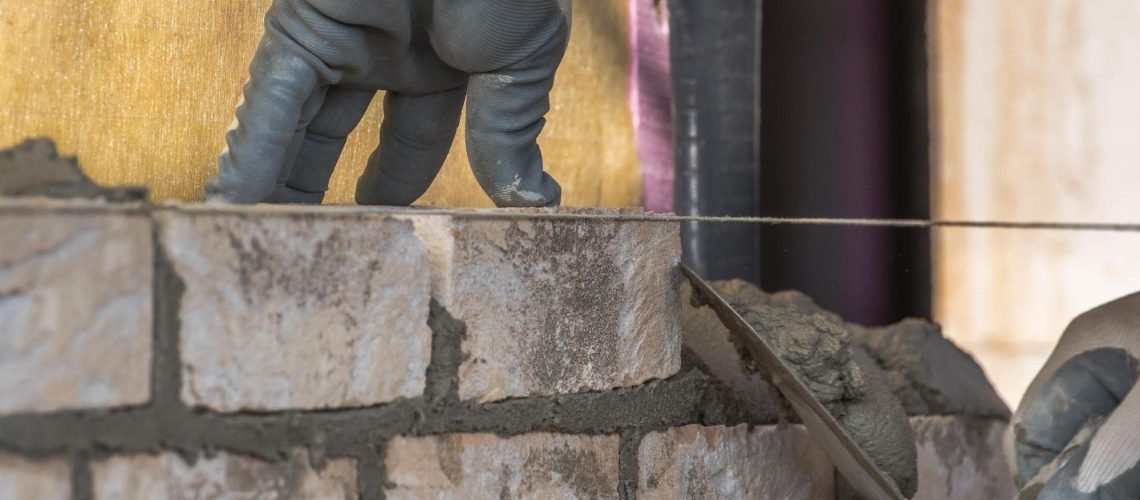 Maçon en formation sur un chantier sur lequel il prépare les fondations d'un bâtiment à l'aide de brique et de béton