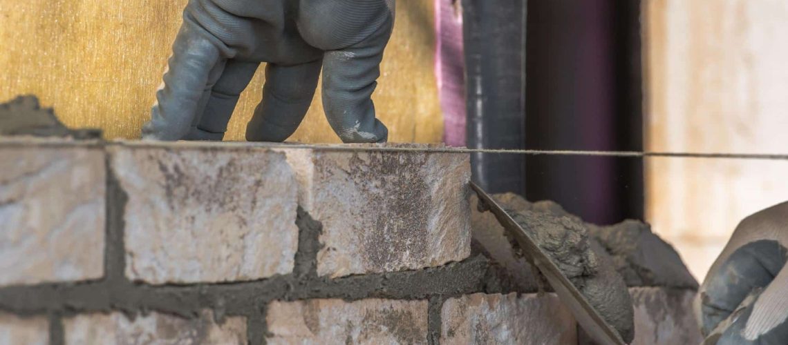Maçon en formation sur un chantier sur lequel il prépare les fondations d'un bâtiment à l'aide de brique et de béton